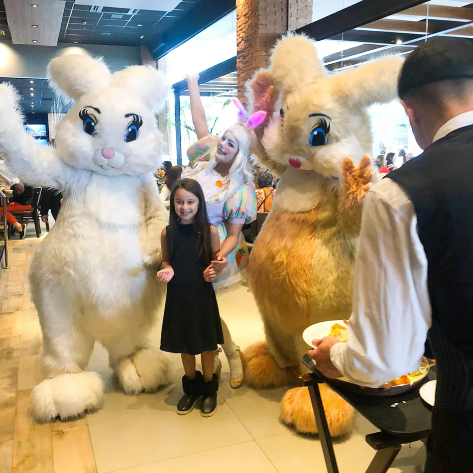 Close de um personagem de Coelho Rosa de pelúcia com uma cesta de ovos de Páscoa coloridos interagindo com crianças em um jardim