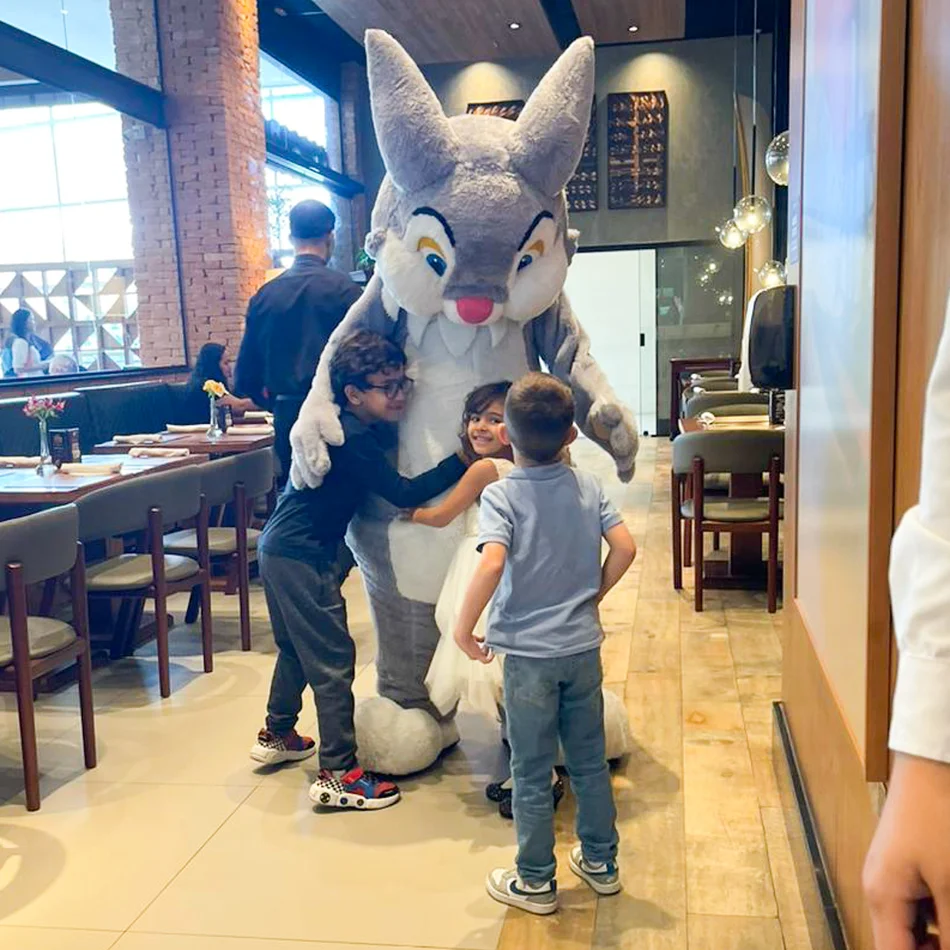 Duas crianças curiosas olhando para um animador de Coelho Cinza sentado no chão com elas durante uma festa infantil de Páscoa